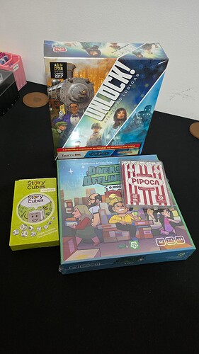 A imagem exibe três jogos de tabuleiro empilhados sobre uma mesa: "Unlock!" no topo, seguido por "Diversão Atrapalhada" e "Pipoca". (Legendado por IA)