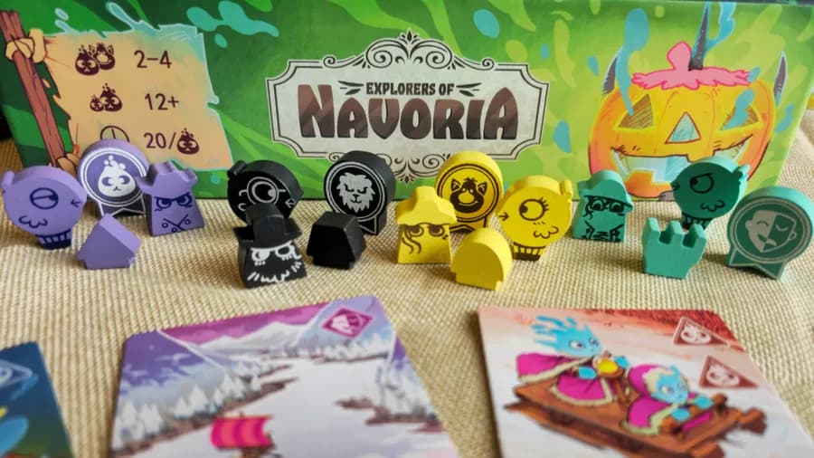 A imagem mostra componentes do jogo "Explorers of Navoria", incluindo várias peças coloridas e cartas em um fundo com a caixa do jogo. (Captioned by AI)